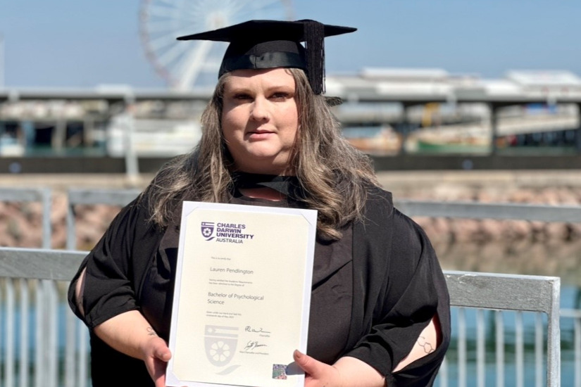 Lauren Pendlington standing in her graduate gown and holding her graduate certificate in Bachelor of Psychological Science.